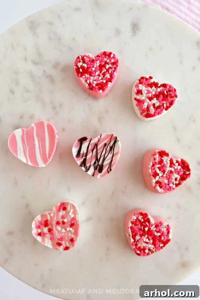 Pink and white homemade chocolate hearts decorated with sprinkles, displayed on a marble cake stand for Valentine's Day.