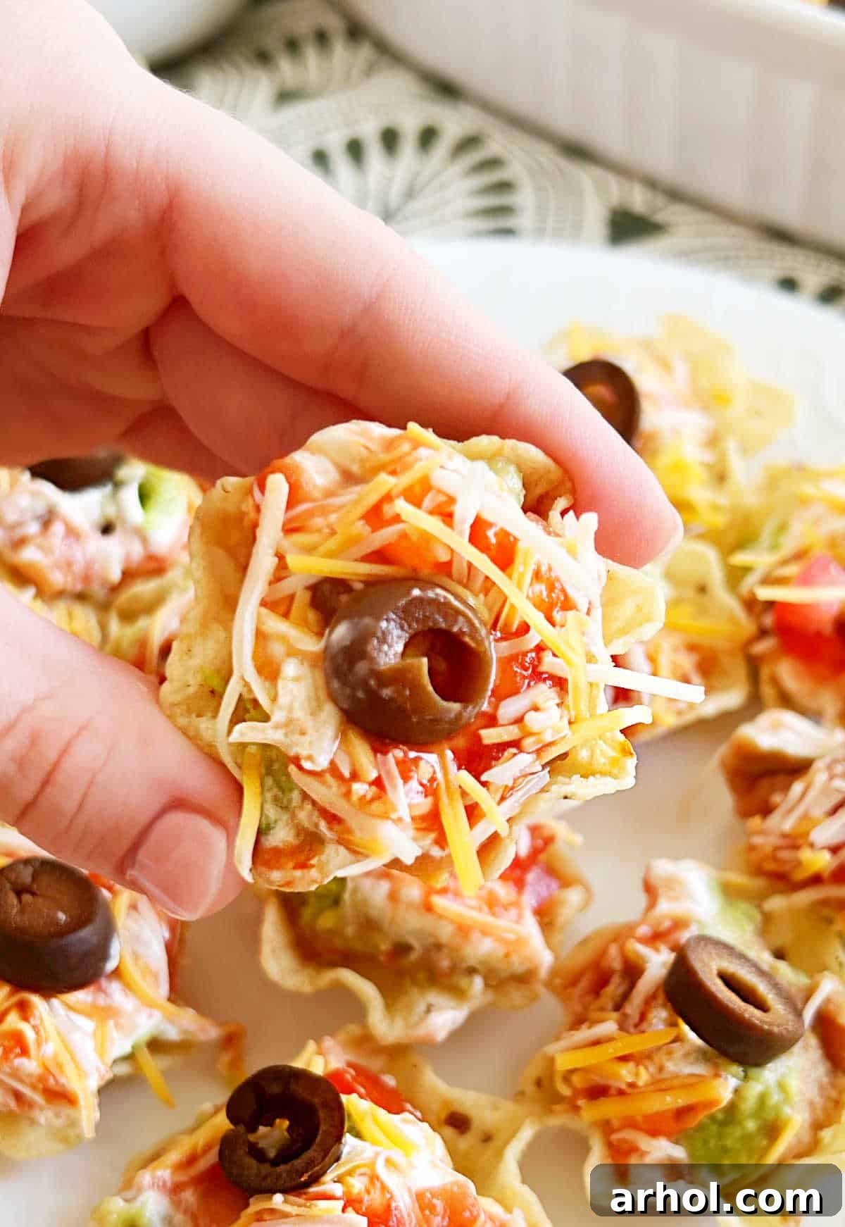 A hand holding an individual seven-layer dip bite in a Tostitos scoop, ready for a delicious snack.
