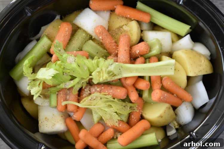 Layering potatoes, baby carrots, and celery stalks over chuck roast in a slow cooker