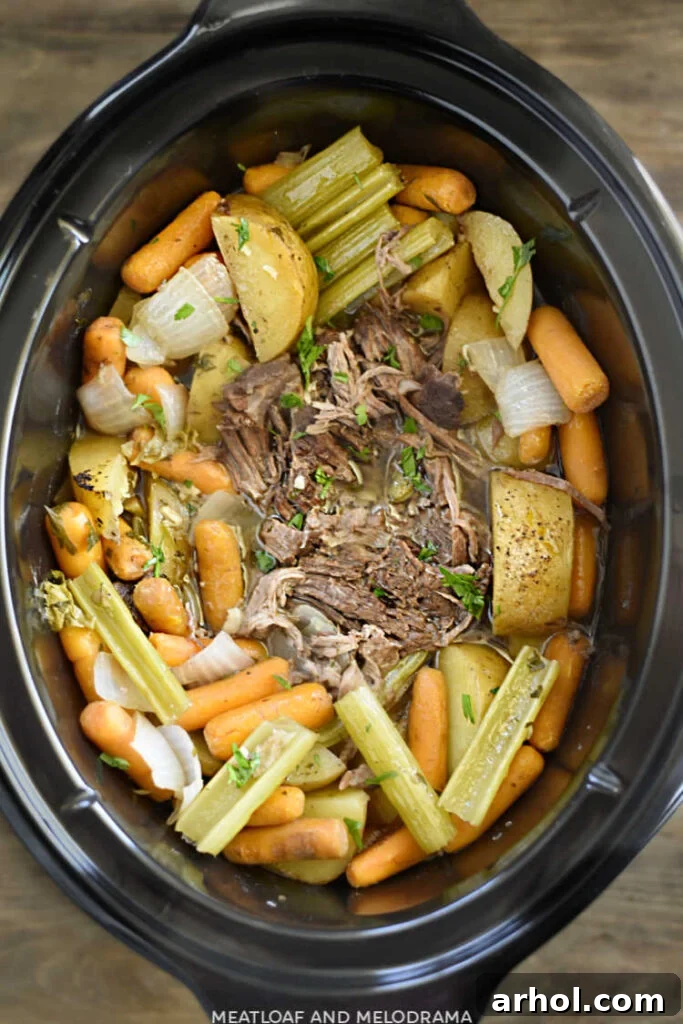 Slow-cooked beef chuck roast with baby carrots, cut potatoes, and celery stalks, topped with fresh parsley in the Crock-Pot