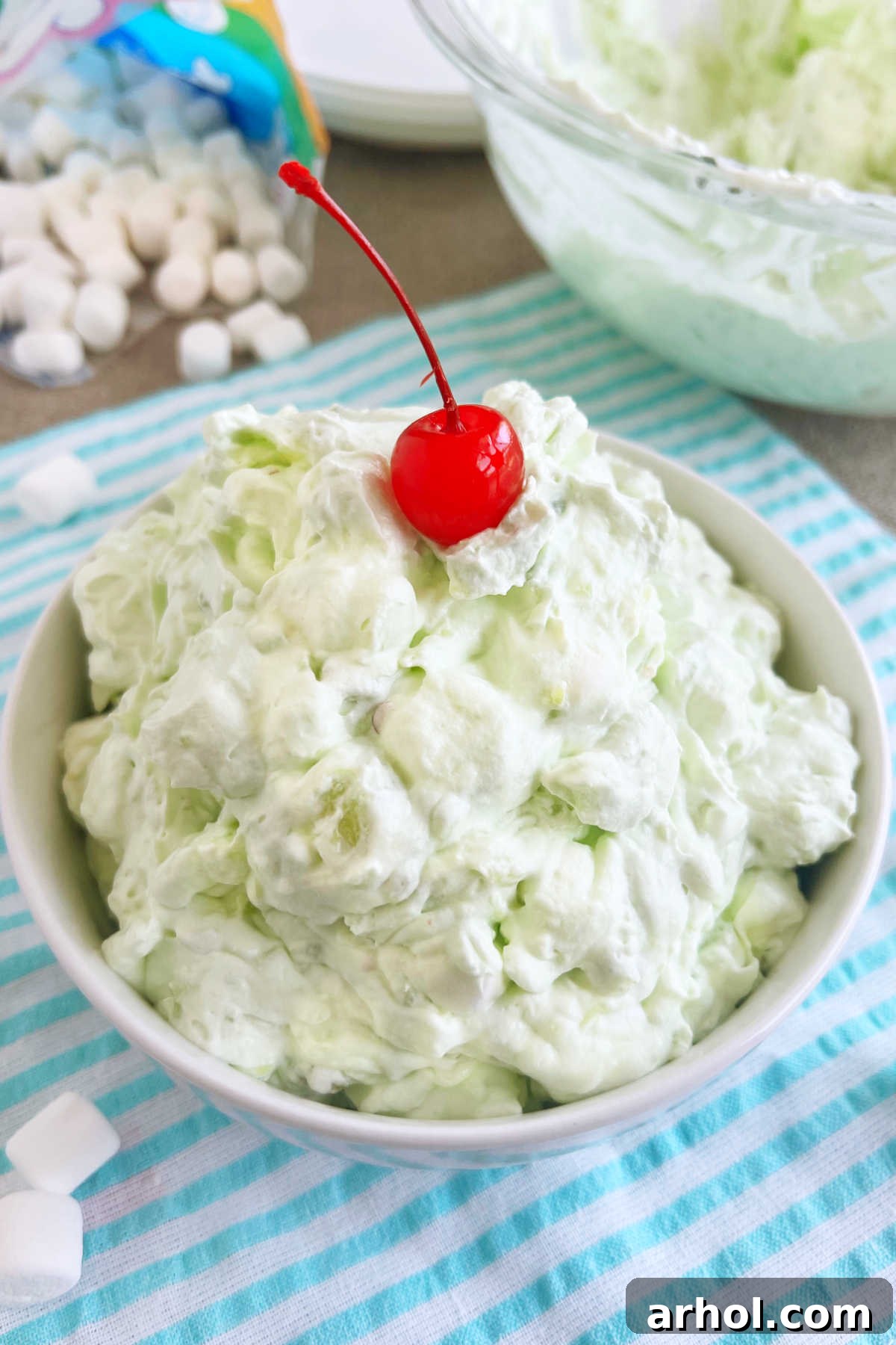 A large bowl of vibrant green pistachio fluff salad, topped with bright red maraschino cherries, ready to be served at a festive gathering.