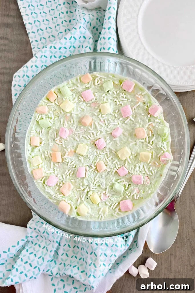 A glass bowl filled with fluffy pistachio salad, adorned with colorful fruit-flavored mini marshmallows, presented as a delightful side or dessert.
