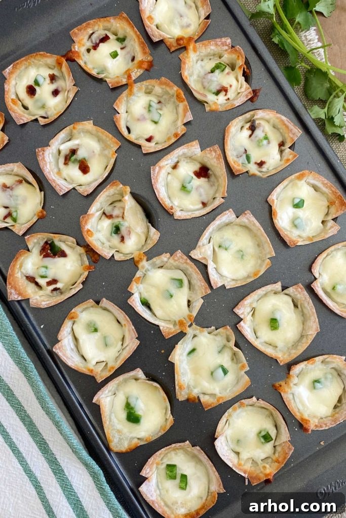 Close-up of baked jalapeno popper wontons in a mini muffin tin, showing crispy edges and melted cheese