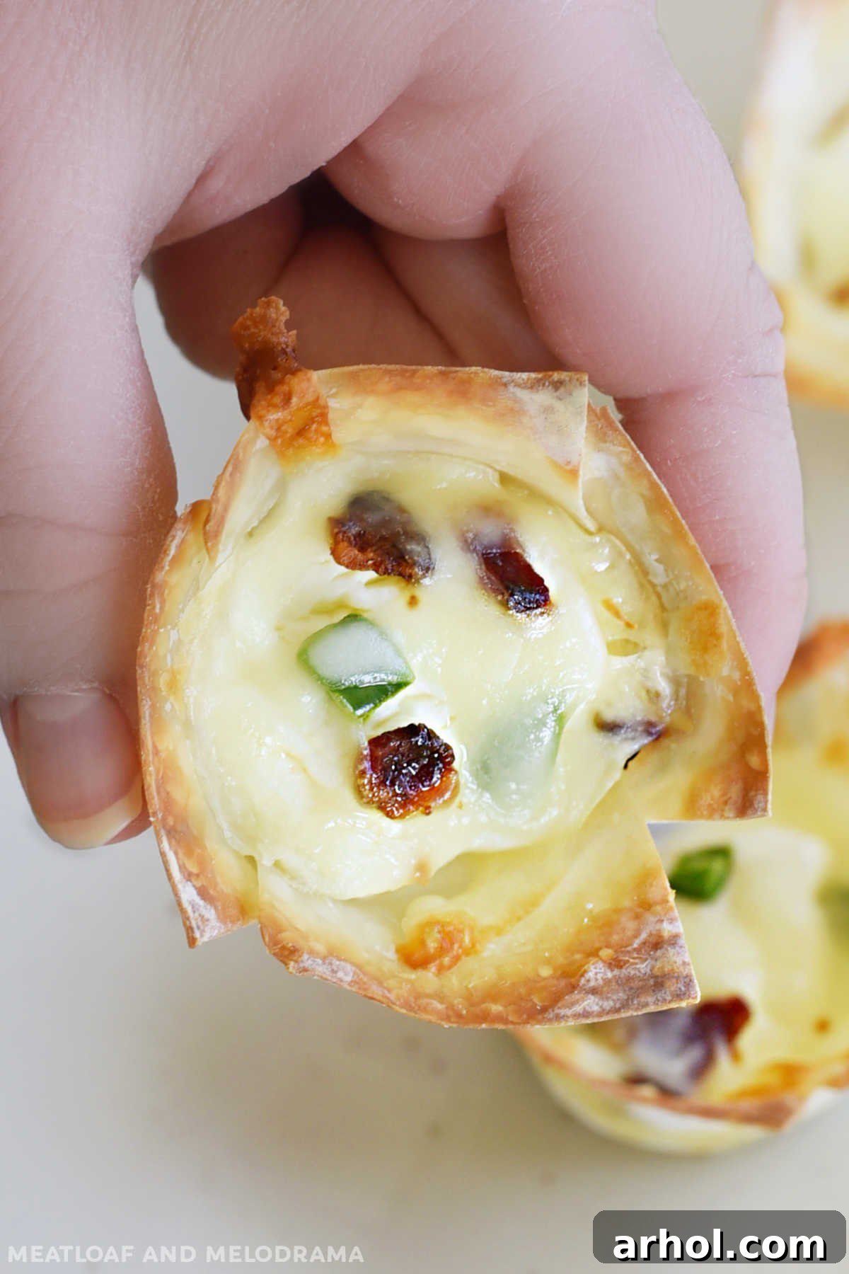 Hand holding a single mini jalapeno popper wonton cup with bacon, highlighting its small size and crispy texture