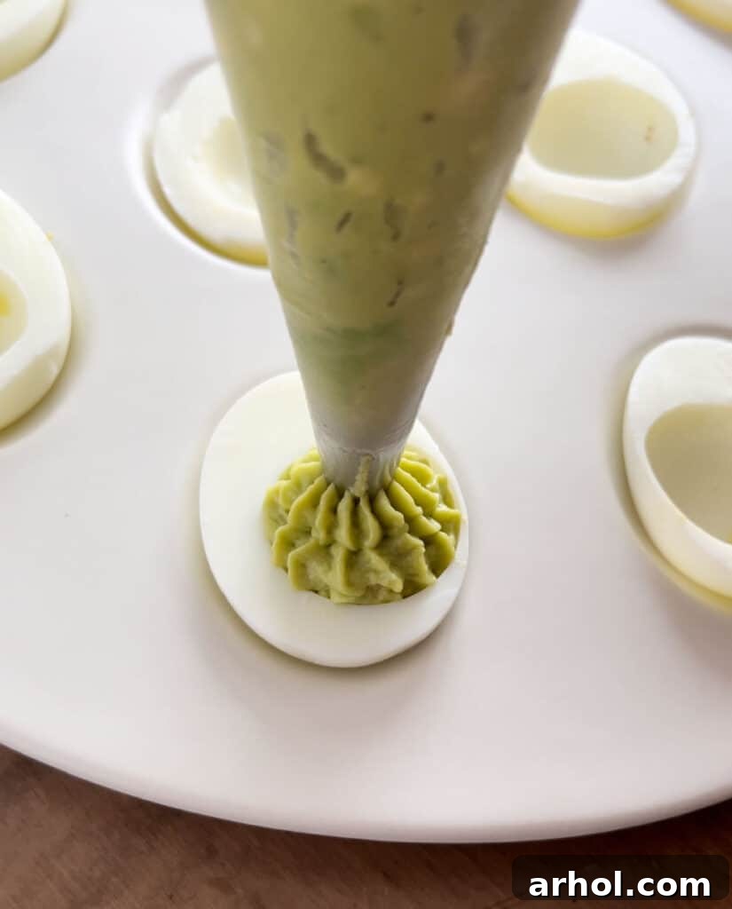 Piping Avocado Filling into Deviled Eggs pipe avocado filling into eggs.