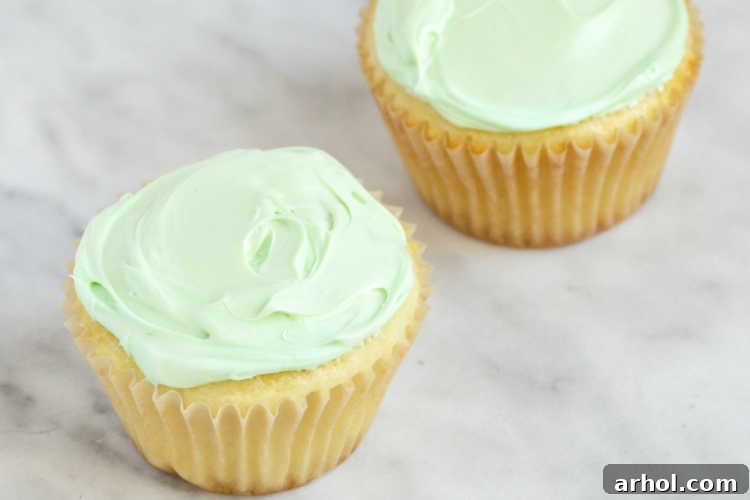 Freshly baked yellow cupcakes topped with a smooth layer of light green frosting, ready for spring decorations.
