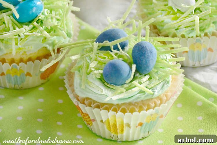 Beautifully decorated Easter cupcakes with edible grass and chocolate candy eggs nestled on top, presented for a spring celebration.