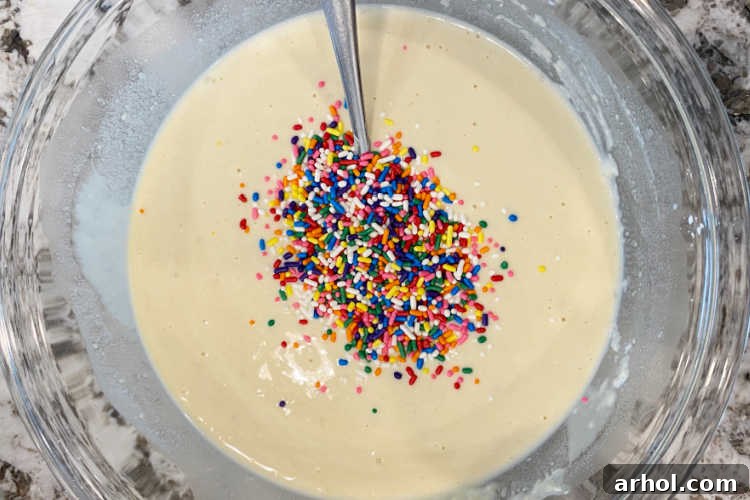 Waffle batter, speckled with rainbow-colored sprinkles, resting in a large mixing bowl, ready for the waffle iron.