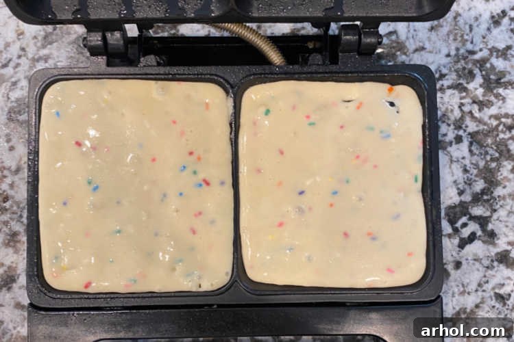 Brightly colored Funfetti waffle batter bubbling and cooking inside a hot waffle iron, showing the melting sprinkles.