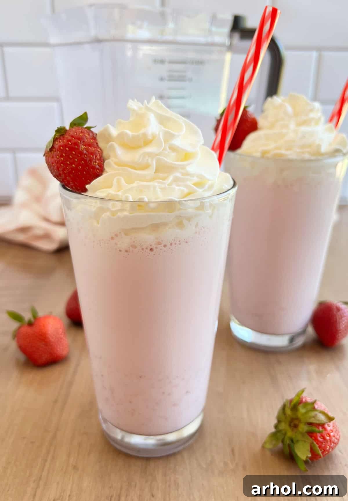 Two tall glasses of homemade strawberry milkshakes topped with whipped cream and fresh strawberries, invitingly placed on a light background.