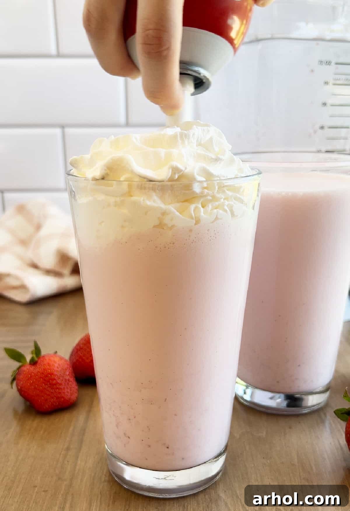 A freshly blended strawberry milkshake in a tall glass, crowned with a generous dollop of whipped cream, ready to be enjoyed.