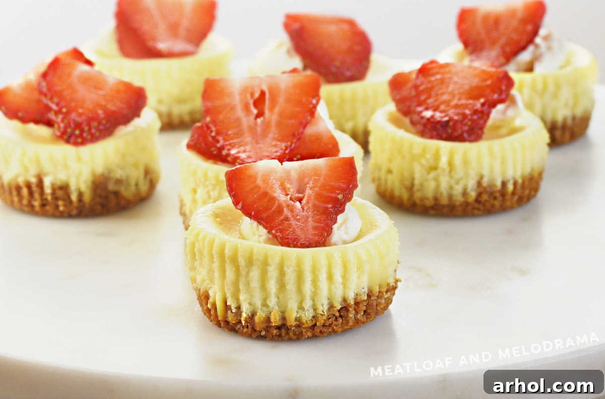 mini cheesecakes with graham cracker crust topped with fresh strawberries on marble cake stand