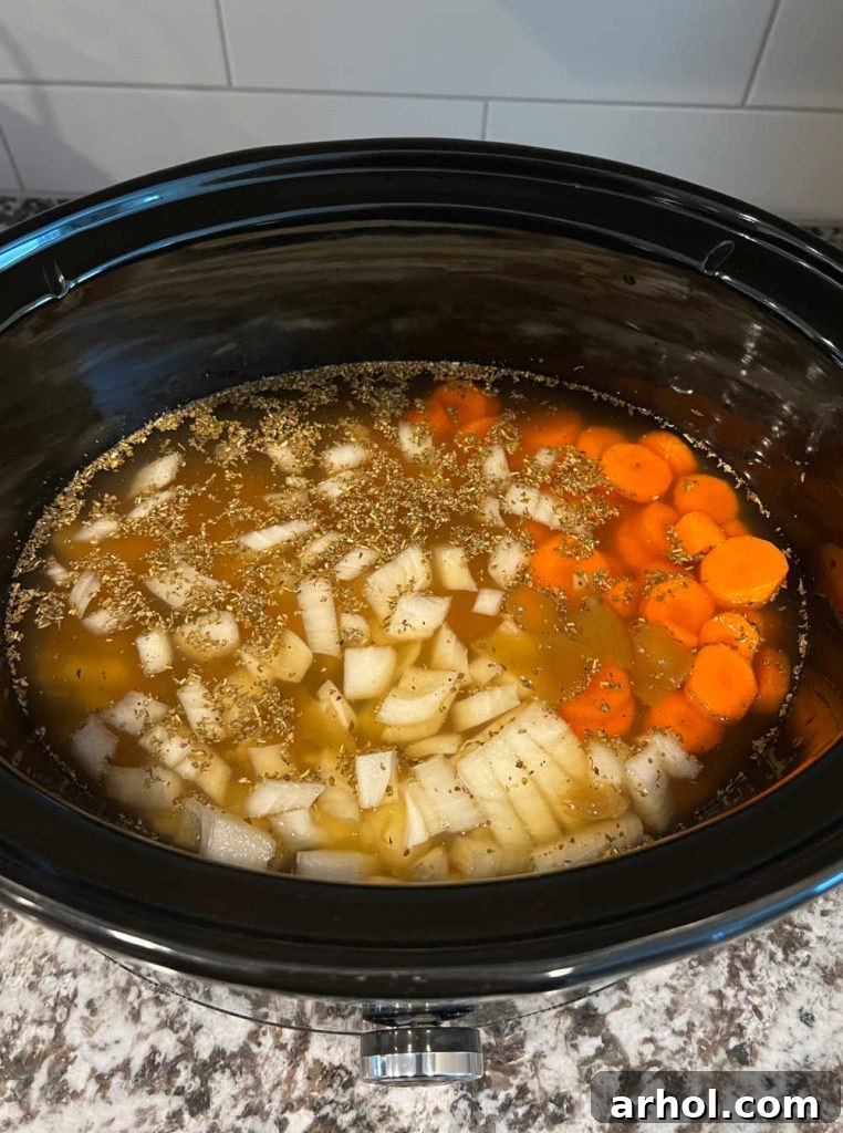 Chopped onions, carrots, and chicken broth added to the slow cooker with chicken.