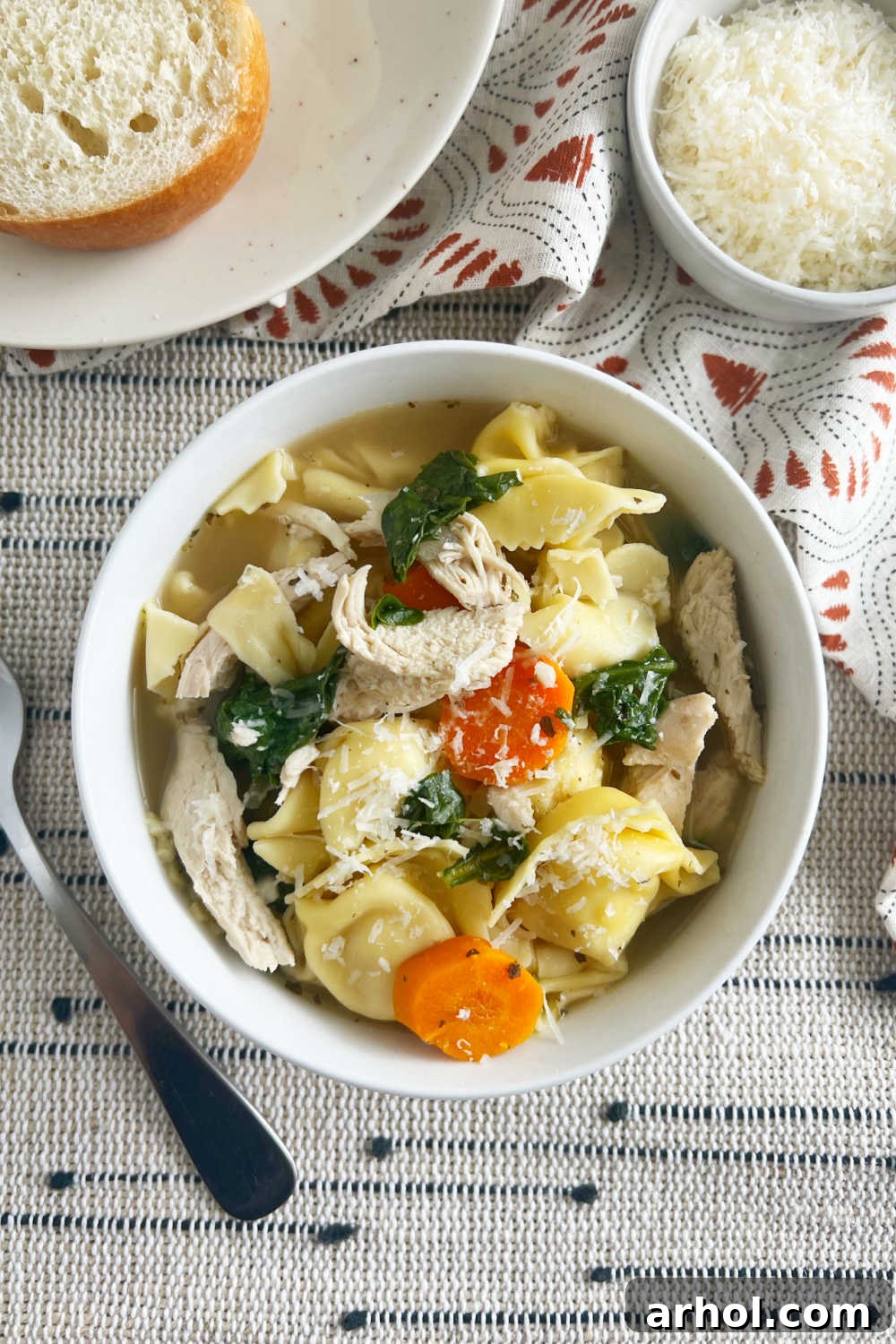 A beautifully presented bowl of Crock Pot Chicken Tortellini Soup with fresh spinach on a rustic table setting.