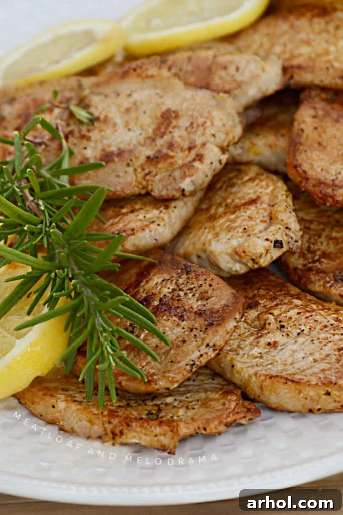 Grilled lemon rosemary pork chops with balsamic glaze on a white platter, garnished with fresh herbs and lemon wedges.