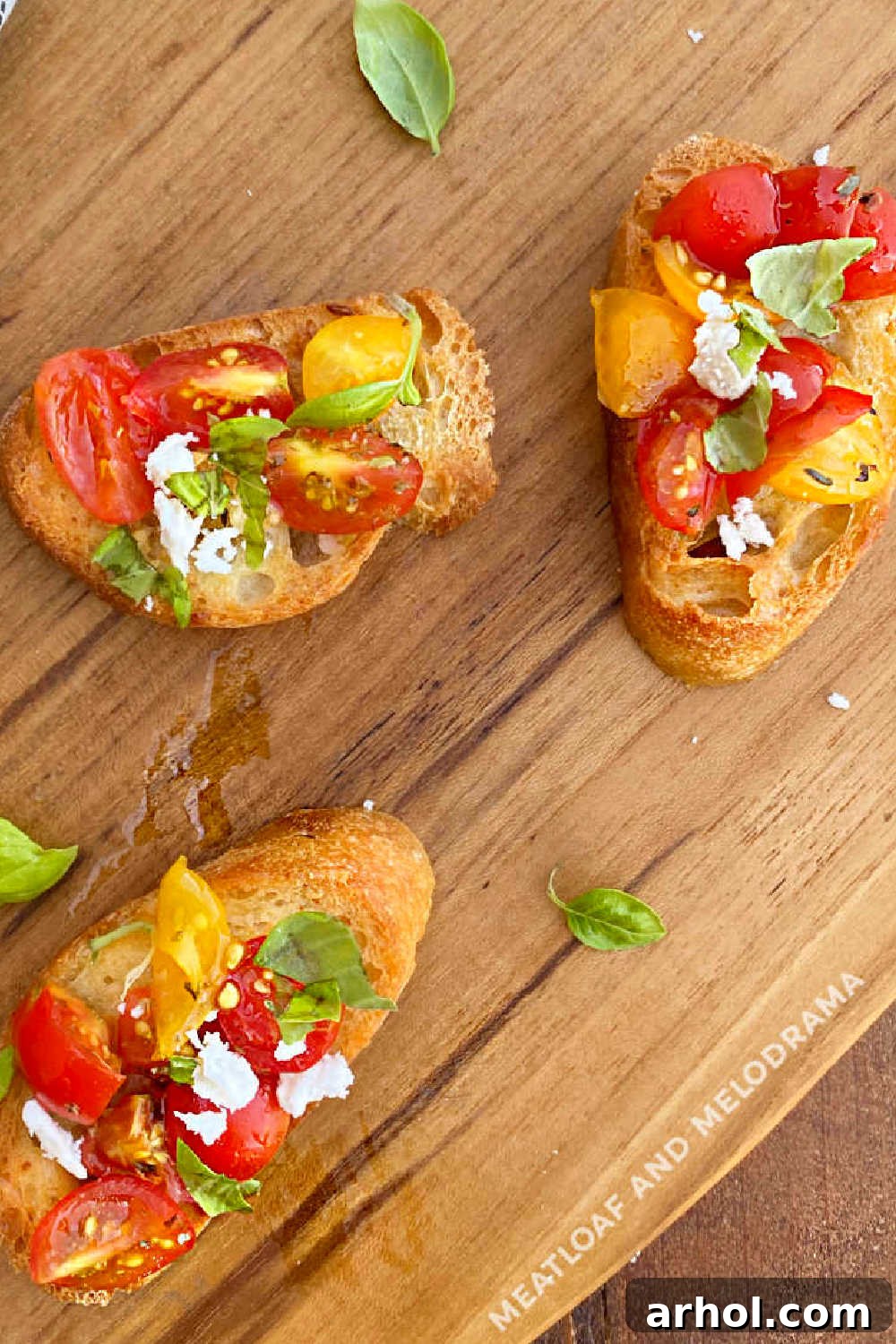 sliced bruschetta with fresh grape tomato and basil leaves topped with feta on wood board