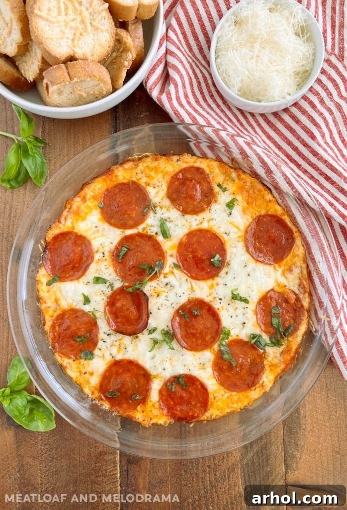 Baked pepperoni dip in a pie plate, bubbling and golden, served on a table with a variety of dippers.