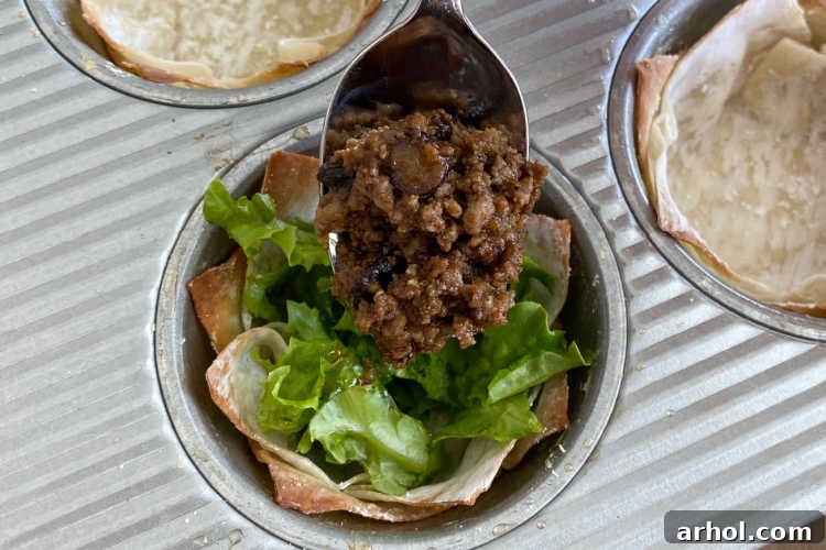 A spoon gently adding cooked and seasoned taco meat into a crispy baked wonton cup, beginning the assembly process.