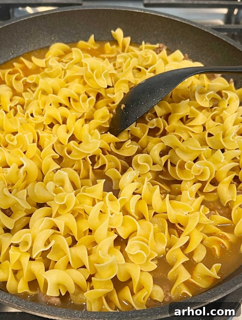 Better-Than-Boxed Ground Beef Stroganoff 5 Egg noodles cooking with beef broth and ground beef in a skillet