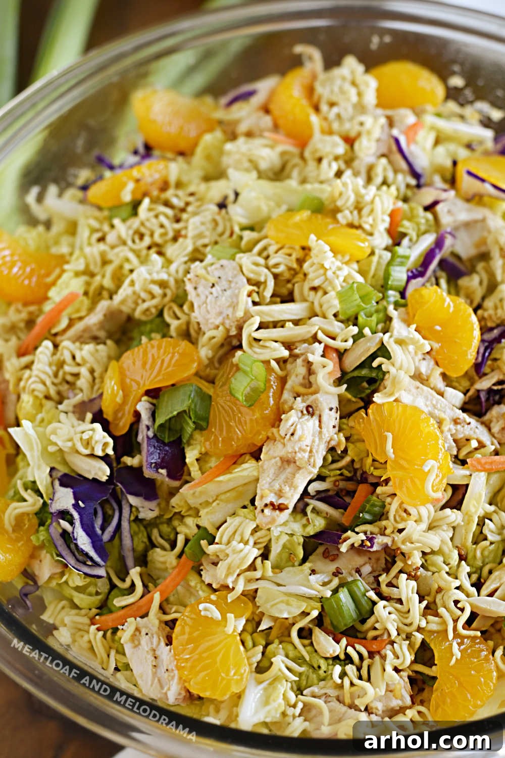 A large serving bowl filled with crunchy Chinese Ramen Chicken Salad, featuring toasted ramen noodles, bright orange mandarin segments, shredded napa cabbage, and visible chicken pieces, making for a colorful and inviting summer dish.