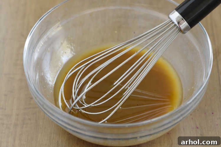 Whisking homemade Asian salad dressing ingredients in a glass mixing bowl, showcasing the vibrant liquid before it's added to the salad.