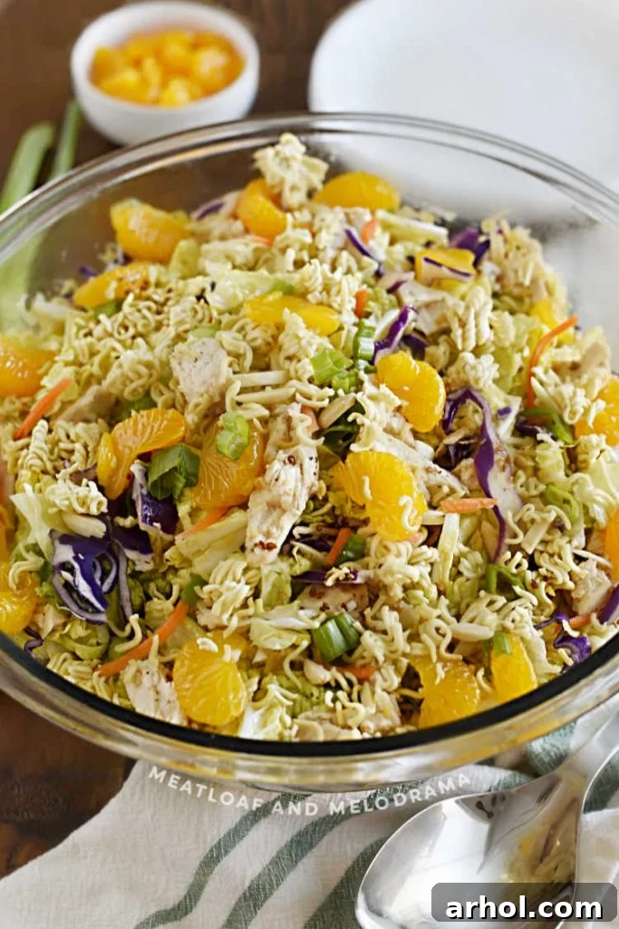 A close-up of a large bowl filled with vibrant Asian chicken salad, featuring shredded napa cabbage, mandarin oranges, and crisp toppings, ready to be served.