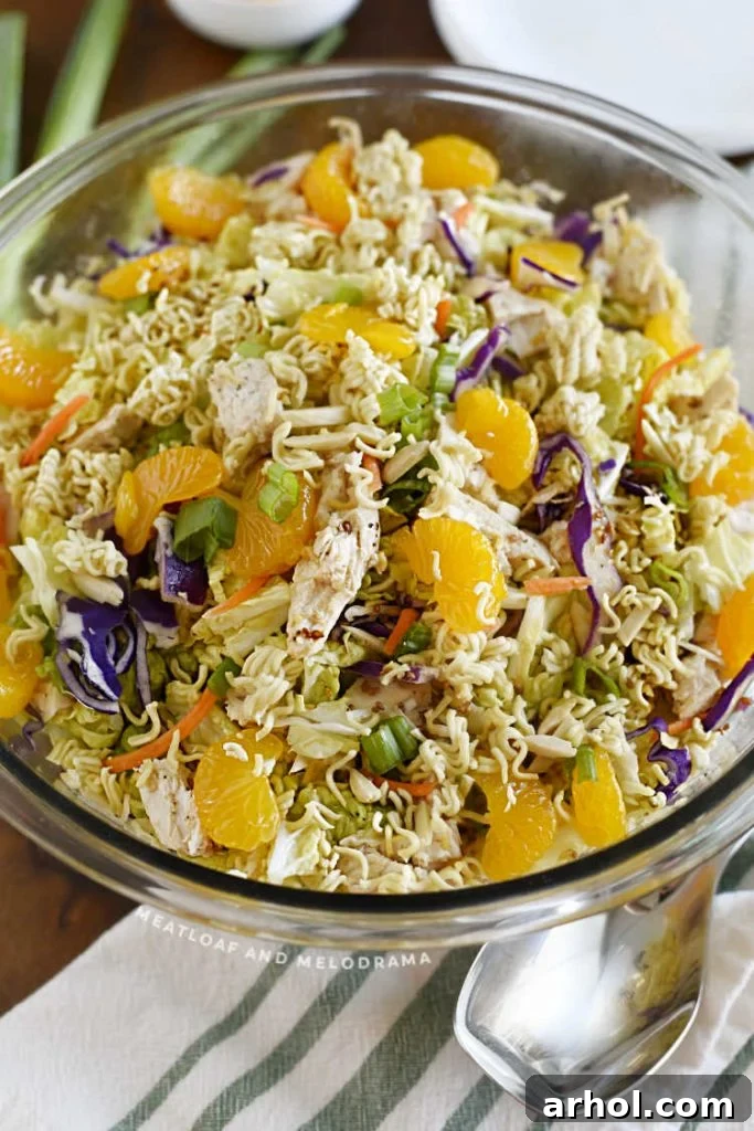 A large glass mixing bowl filled with vibrant ramen chicken salad, showcasing the colorful ingredients like cabbage, mandarin oranges, and toasted noodles, ready to be served.