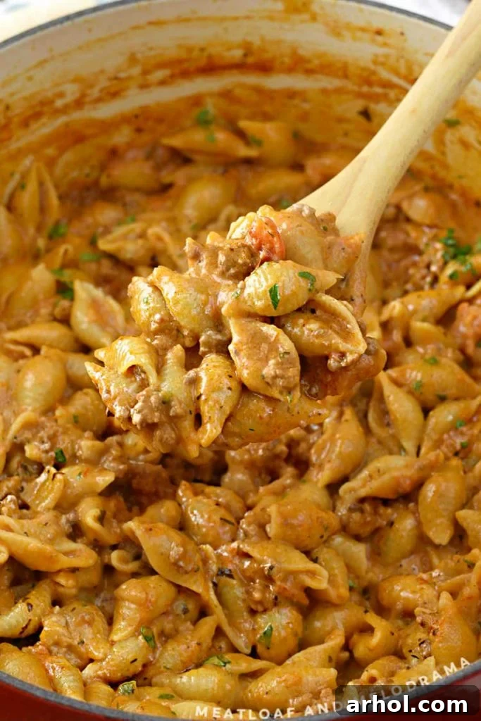 A close-up of ground beef and shell pasta on a wooden spoon, showcasing the creamy sauce.