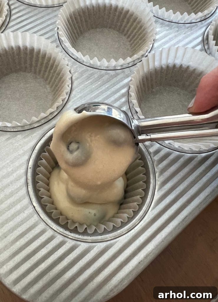 Spoon muffin batter into muffin cups lined with paper liners using a cookie scoop.
