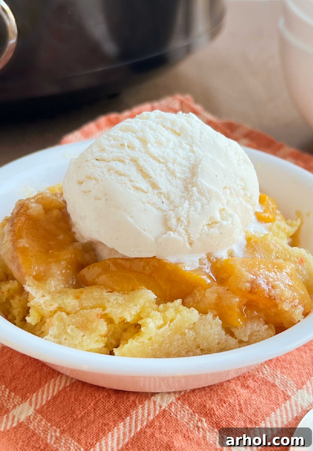A bowl of Crock Pot Peach Cobbler topped with a scoop of vanilla ice cream, ready to be enjoyed.
