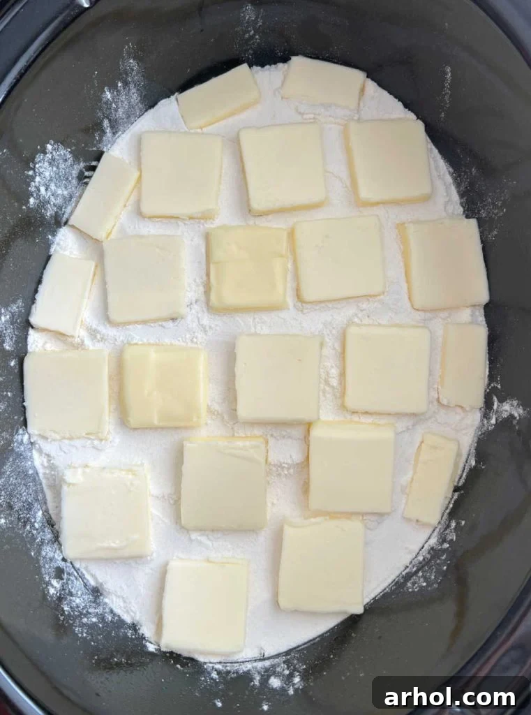 Layers of cake mix and pats of butter evenly spread over canned peaches in a slow cooker, ready for cooking.