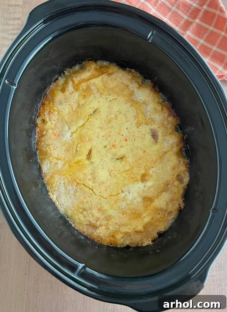 The finished peach cobbler, bubbling around the edges and with a golden-brown crust, visible in the slow cooker.
