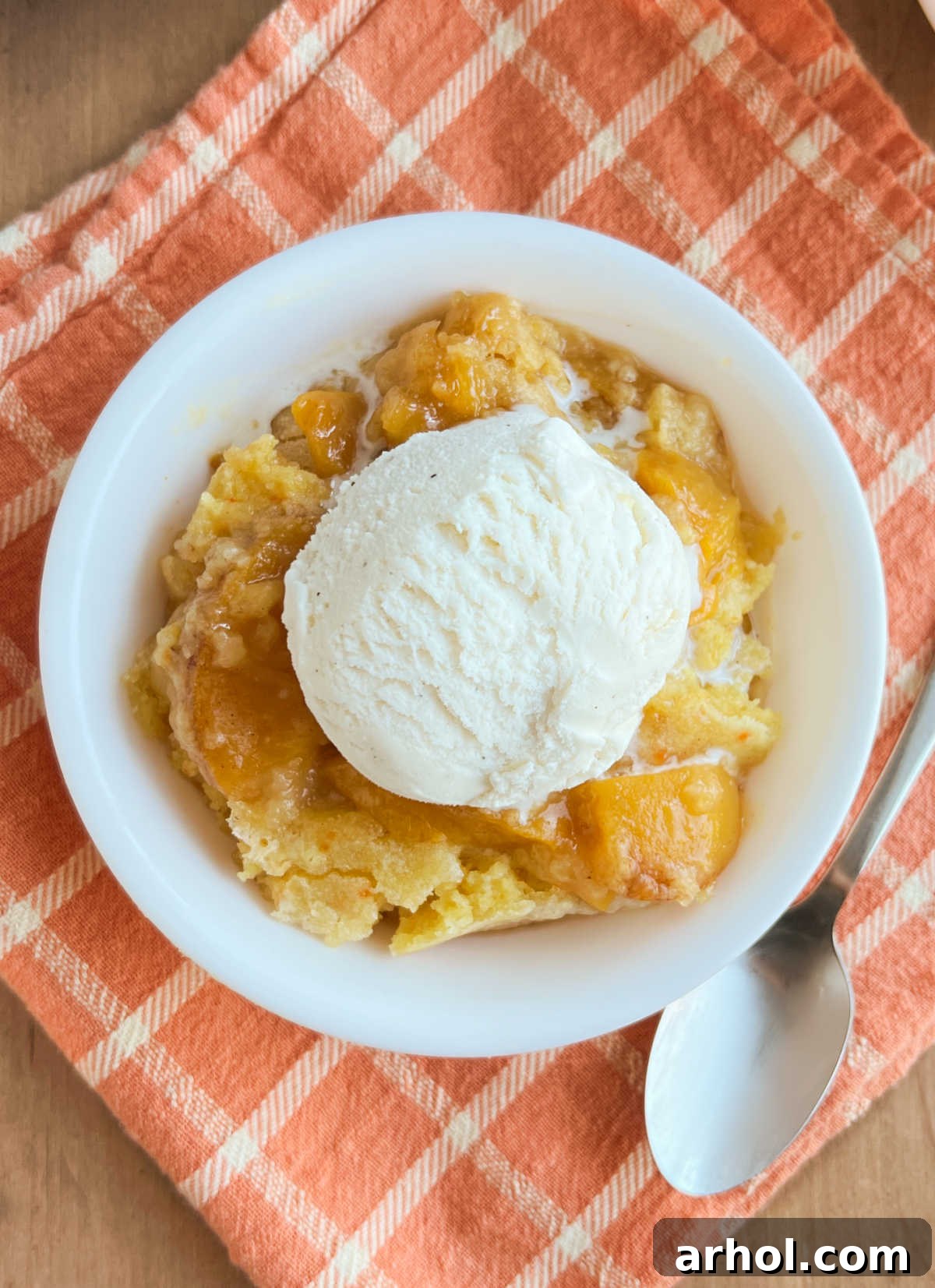 A serving of cake mix peach cobbler with a generous scoop of vanilla ice cream melting on top, garnished with a mint leaf.