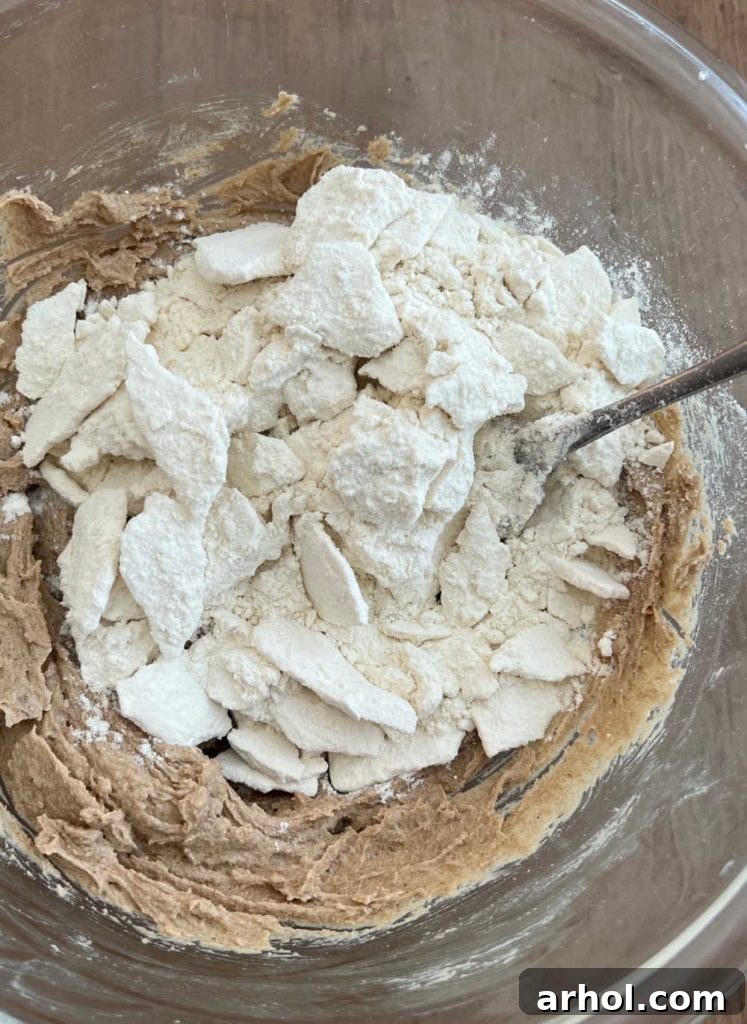 The process of stirring heat-treated flour into creamed butter and brown sugar within a mixing bowl to form the cookie dough base.
