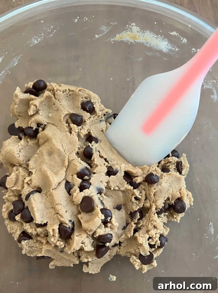 Semi-sweet chocolate chips being stirred into the prepared edible cookie dough in a mixing bowl.