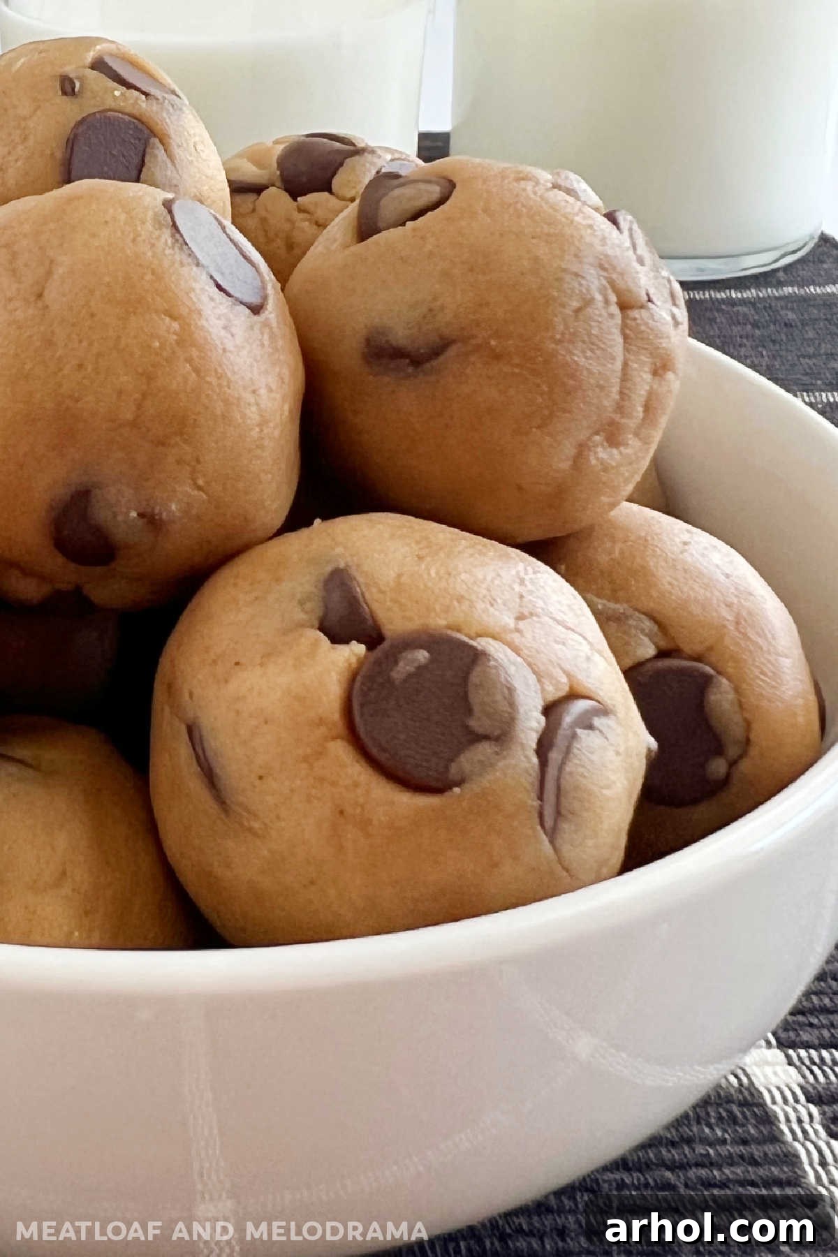 A close-up shot of no-bake chocolate chip cookie dough balls, firm and ready to eat, with a glass of milk in the background.