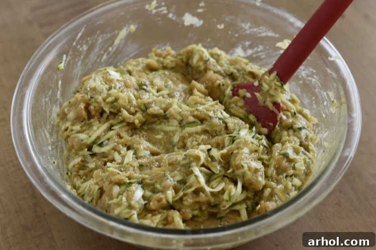 Freshly grated zucchini mixed with the wet bread batter in a large mixing bowl, showcasing the consistency before baking.