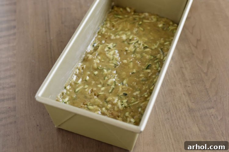 The zucchini bread batter neatly poured into a greased metal loaf pan, ready to be placed in the oven.