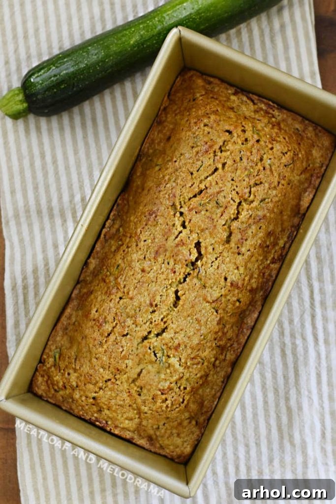 A freshly baked golden-brown zucchini bread loaf cooling in a metal pan on a wire rack.