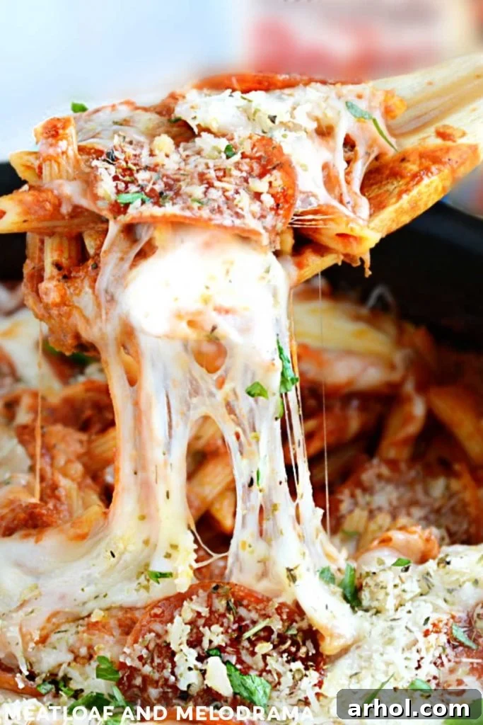 Close-up of penne pasta with luscious, melted, and stretchy mozzarella cheese being pulled from the skillet.