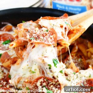 A serving spoon lifting cheesy pepperoni pizza pasta from a skillet, showcasing its deliciousness.