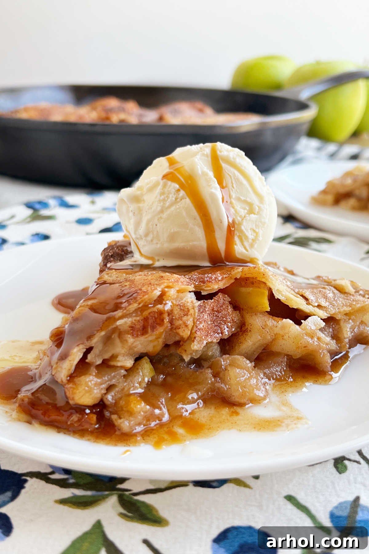 A delectable slice of cast iron skillet apple pie adorned with a generous scoop of vanilla ice cream, served on a pristine white plate.