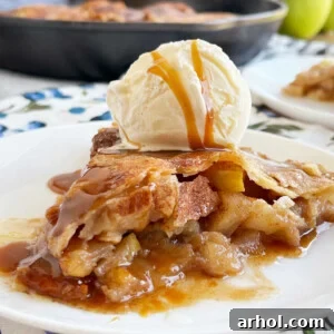 A delicious slice of skillet apple pie with vanilla ice cream and caramel sauce on a plate, ready to be enjoyed.