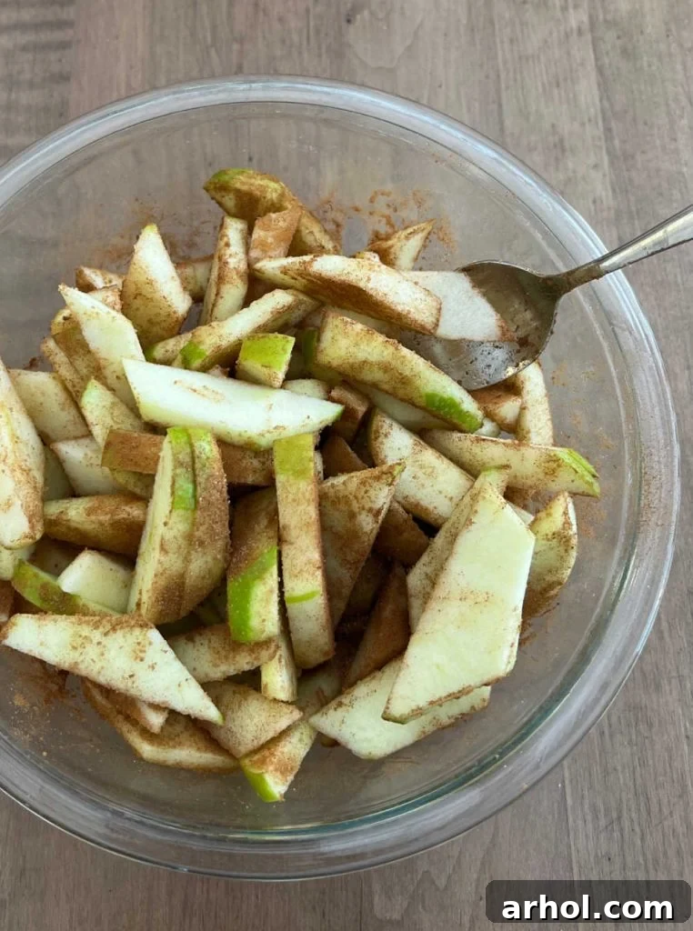 Sliced apples coated in a brown sugar and cinnamon mixture resting in a mixing bowl, ready for the pie.