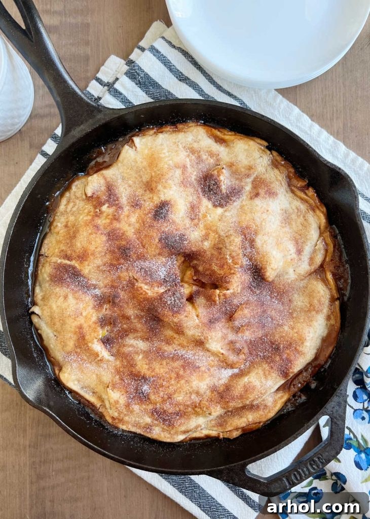 A freshly baked apple pie in a cast iron skillet, cooling on a wooden table, emitting steam.
