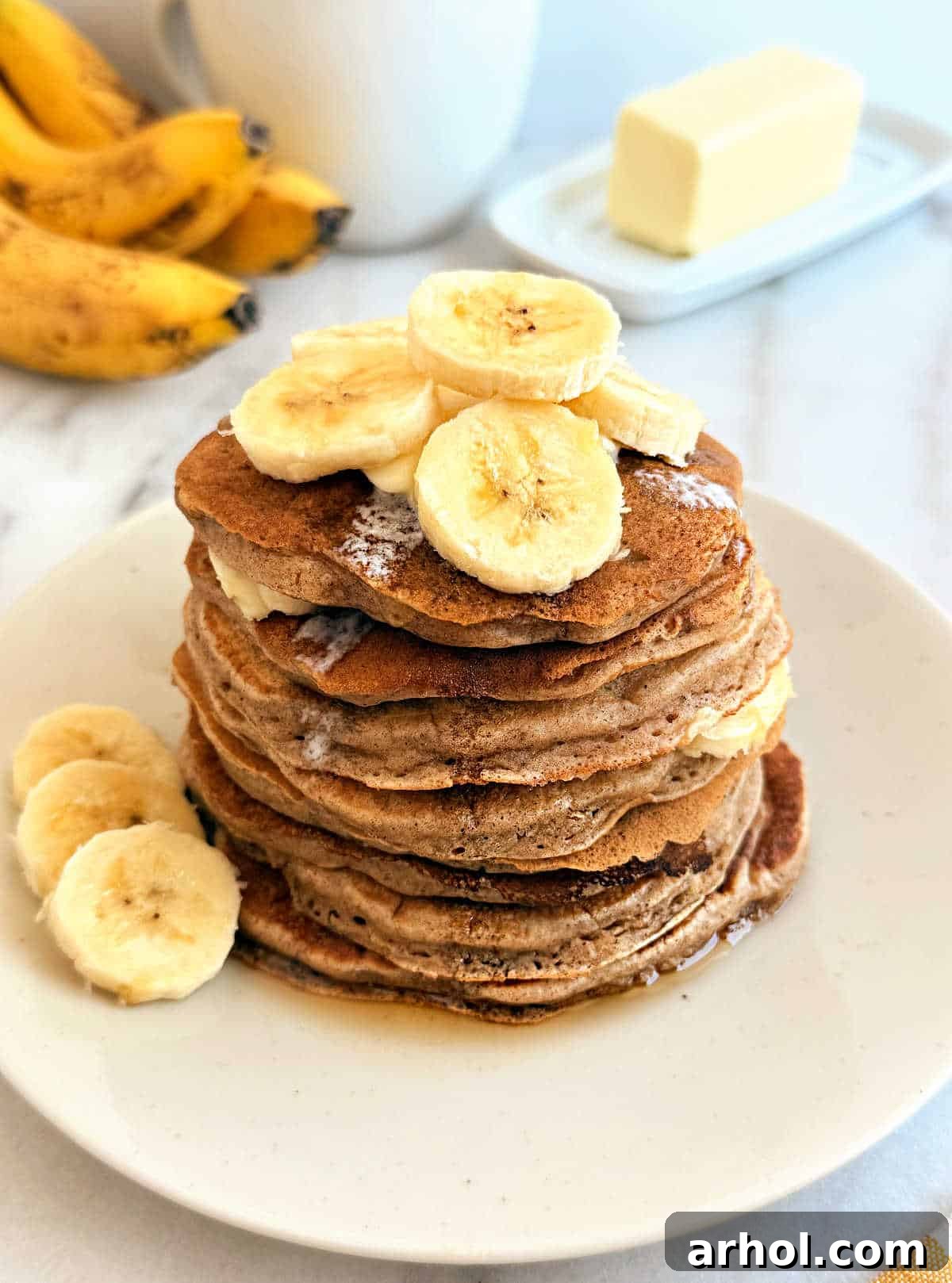 Fluffy banana cinnamon pancakes stacked high, topped with maple syrup and fresh banana slices, ready to be enjoyed for breakfast.