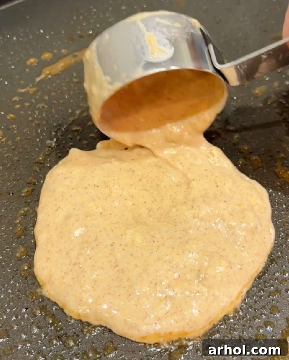 Pouring pancake batter onto a hot griddle, illustrating the even distribution needed for perfectly round banana pancakes.