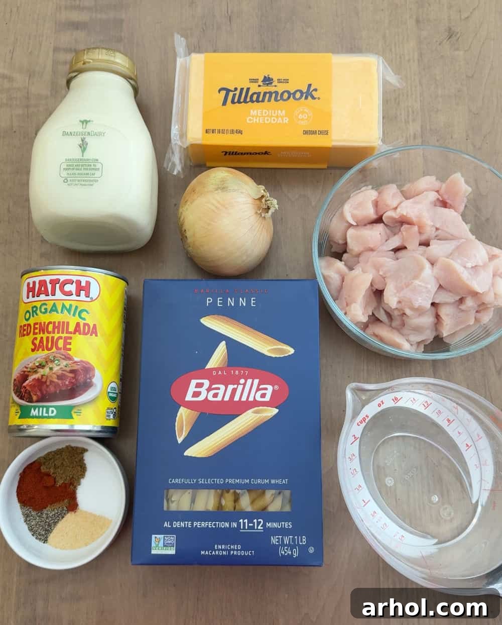 Key ingredients laid out for one-pan chicken enchilada pasta: cubed chicken, penne, various spices, chopped onion, heavy cream, shredded cheese, water, and a can of red enchilada sauce.