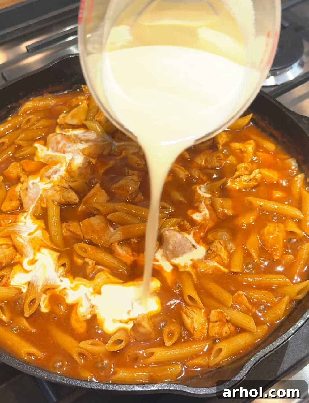 Pouring heavy cream into the simmering chicken enchilada pasta mixture, enhancing its richness and creaminess.