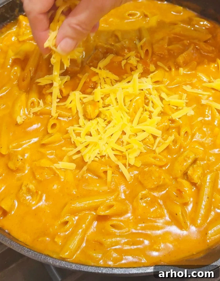 Adding a generous amount of shredded cheddar and Mexican blend cheese to the hot pasta, allowing it to melt into a gooey, savory finish.